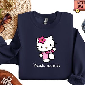 Puede incluir: Sudadera azul marino con un personaje de dibujos animados con un vestido y una flor rosas, con el texto "Your name" en blanco. El dise&ntilde;o est&aacute; centrado en la parte delantera. Sudadera de la marca Gildan.