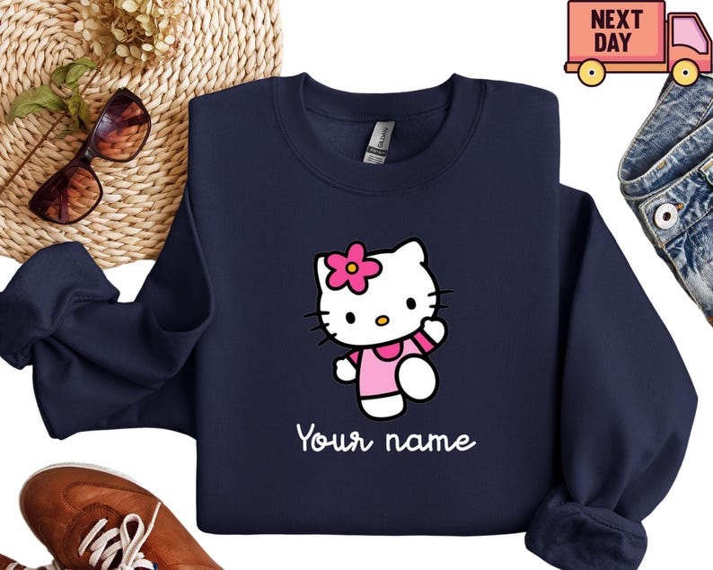 Puede incluir: Sudadera azul marino con un personaje de dibujos animados con un vestido y una flor rosas, con el texto "Your name" en blanco. El dise&ntilde;o est&aacute; centrado en la parte delantera. Sudadera de la marca Gildan.