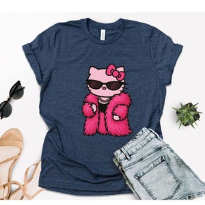 Puede incluir: Camiseta azul marino con un personaje de dibujos animados de Hello Kitty con gafas de sol y un abrigo de piel rosa. El gr&aacute;fico est&aacute; centrado en la camiseta. La camiseta se combina con pantalones cortos vaqueros azules, gafas de sol y sandalias.