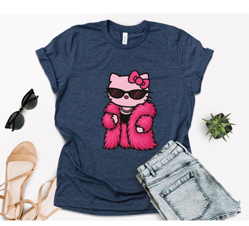 Puede incluir: Camiseta azul marino con un personaje de dibujos animados de Hello Kitty con gafas de sol y un abrigo de piel rosa. El gr&aacute;fico est&aacute; centrado en la camiseta. La camiseta se combina con pantalones cortos vaqueros azules, gafas de sol y sandalias.