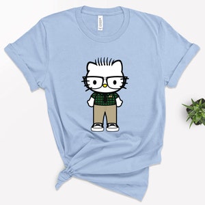 May include: Light blue t-shirt with a cartoon image of Hello Kitty wearing glasses, a green plaid shirt, and khaki pants.