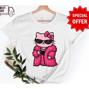 Puede incluir: Camiseta blanca con un gato de dibujos animados rosa con gafas de sol y un abrigo de piel rosa. El gato tiene un lazo rosa y un collar. La camiseta tiene el texto "NEXT DAY" y un icono de cami&oacute;n.