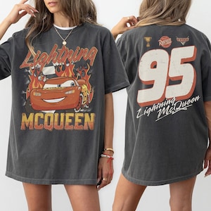 May include: Dark gray Lightning McQueen t-shirt. The front features a graphic of the character with flames and the text "Lightning McQueen". The back displays the number "95" with "Lightning McQueen" text.