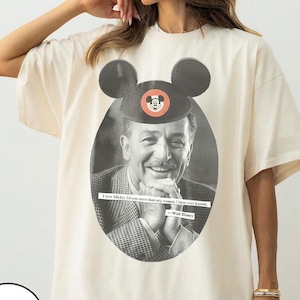 May include: Ivory-colored t-shirt featuring a black and white image of Walt Disney wearing a Mickey Mouse hat. The shirt includes the quote, "I love Mickey Mouse more than any woman I have ever known."