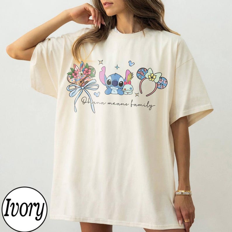 Puede incluir: Camiseta de color marfil con un gr&aacute;fico colorido de Stitch, un lazo floral y diademas con orejas de rat&oacute;n. El texto "Ohana means family" est&aacute; escrito en cursiva. La camiseta es de corte holgado.