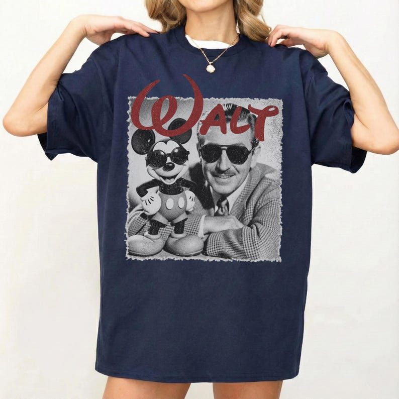 May include: Navy blue t-shirt featuring a black and white image of Walt Disney with Mickey Mouse wearing sunglasses. The word "WALT" is printed in red above the image. The shirt is a classic crew neck style.