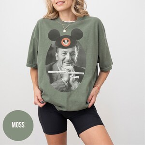 May include: An olive green t-shirt featuring a black and white image of Walt Disney wearing a Mickey Mouse hat. The shirt includes the quote, "I love Mickey Mouse more than any woman I have ever known."