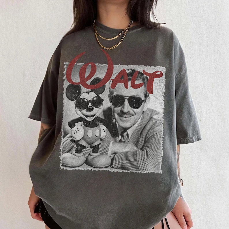 May include: Gray t-shirt featuring a black and white image of Mickey Mouse and Walt Disney with the word "WALT" in red. The shirt has short sleeves and a relaxed fit, suitable for casual wear.