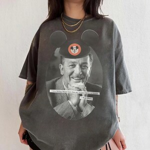 May include: Dark gray t-shirt featuring a black and white image of Walt Disney with a Mickey Mouse hat. The shirt includes the quote "I love Mickey Mouse more than any woman I have ever known." and the Walt Disney signature.