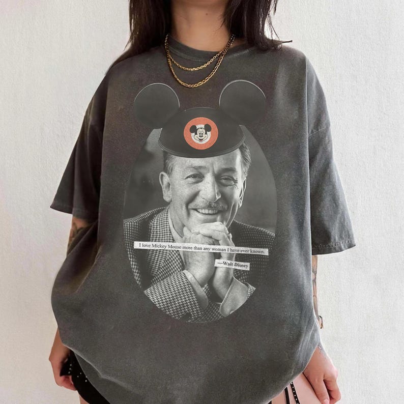 May include: Dark gray t-shirt featuring a black and white image of Walt Disney with a Mickey Mouse hat. The shirt includes the quote "I love Mickey Mouse more than any woman I have ever known." and the Walt Disney signature.
