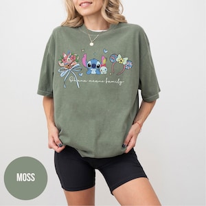 Puede incluir: Camiseta verde oliva con un gr&aacute;fico colorido que presenta a Stitch, elementos florales y orejas de rat&oacute;n. El texto "Ohana means family" est&aacute; escrito en cursiva. La camiseta se combina con pantalones cortos negros.