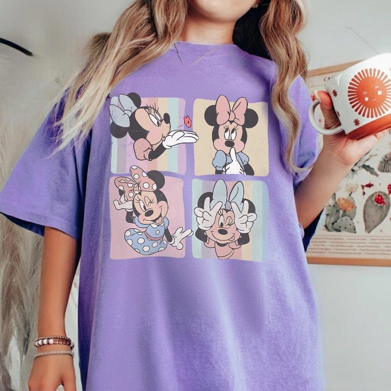 May include: A purple t-shirt featuring a four-panel design of Minnie Mouse in various poses. Each panel has a different background color. Minnie is wearing different outfits and bows. The shirt is a comfortable, oversized fit.