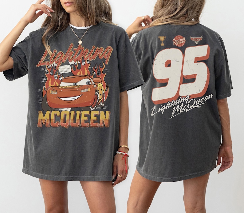 May include: Dark gray Lightning McQueen t-shirt. The front features a graphic of the character with flames and the text "Lightning McQueen". The back displays the number "95" with "Lightning McQueen" text.