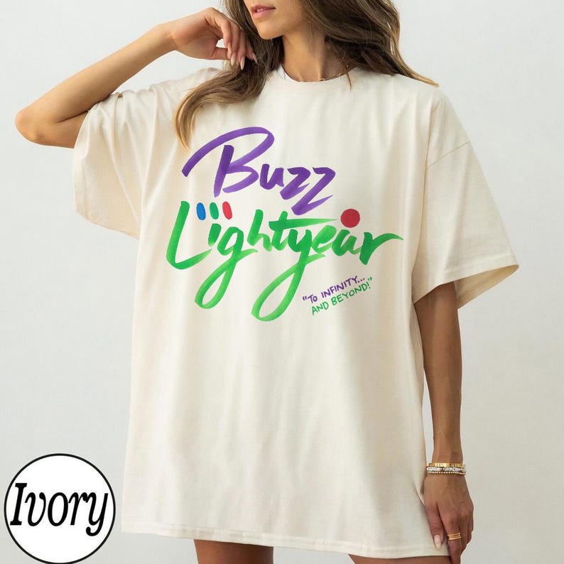 Puede incluir: Una camiseta de manga corta color marfil con el texto morado Buzz y el texto verde Lightyear. El dise&ntilde;o incluye peque&ntilde;os c&iacute;rculos azules, rojos y verdes, junto con el texto verde To infinity... and beyond! impreso en la parte delantera.