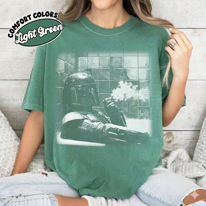 May include: A light green short-sleeve t-shirt featuring a graphic print of a helmeted character in a bathtub with smoke rising. The text Comfort Colors Light Green is printed in the upper left corner. The shirt has a crew neckline and a relaxed fit.