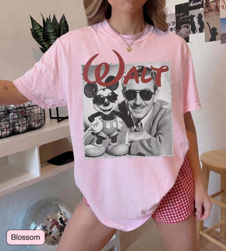 May include: A light pink t-shirt featuring a vintage-style graphic of Mickey Mouse and Walt Disney, with the word "Walt" in red script. The shirt is a soft, comfortable material.