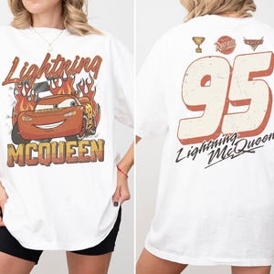 May include: White t-shirt featuring a distressed graphic of Lightning McQueen with flames and text. The back of the shirt displays the number 95, a trophy, and the text "Lightning McQueen".