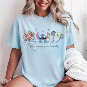 Puede incluir: Camiseta azul claro con un gr&aacute;fico de Stitch y Angel, detalles florales y lazos, y el texto "Ohana means family". El dise&ntilde;o incluye diademas con orejas de rat&oacute;n. Una camiseta casual y c&oacute;moda.