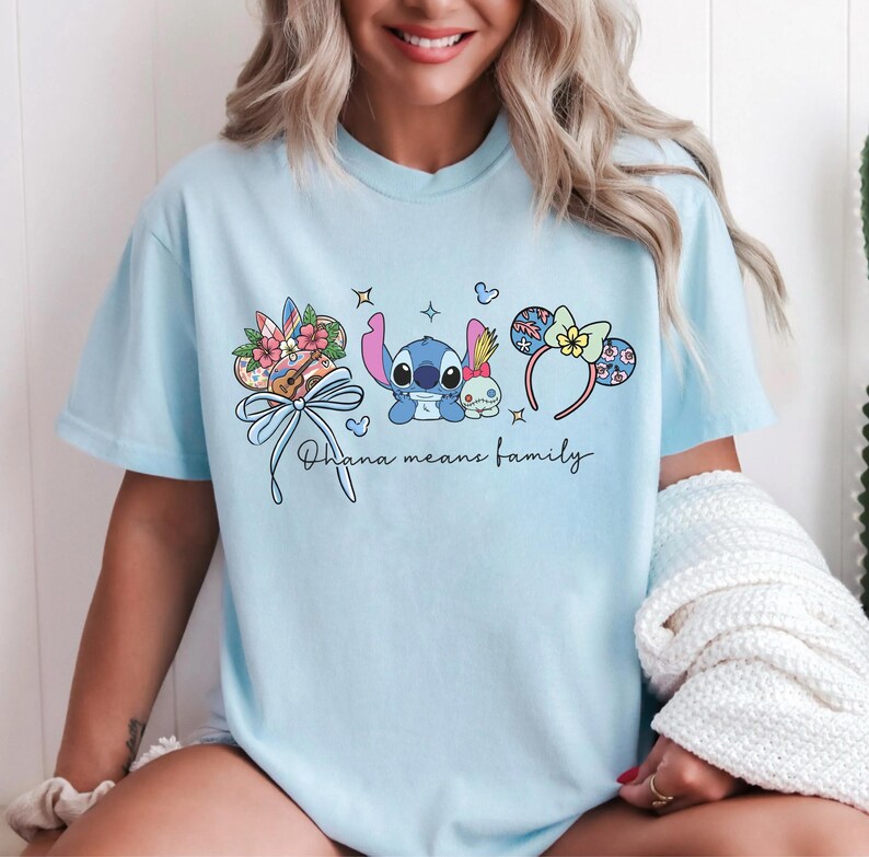 Puede incluir: Camiseta azul claro con un gr&aacute;fico de Stitch y Angel, detalles florales y lazos, y el texto "Ohana means family". El dise&ntilde;o incluye diademas con orejas de rat&oacute;n. Una camiseta casual y c&oacute;moda.