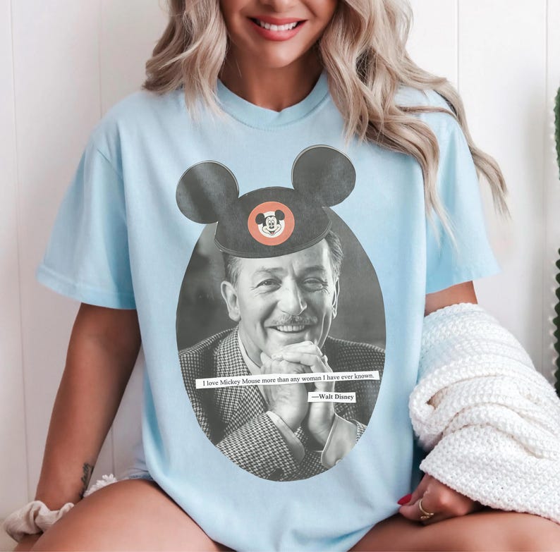 May include: Light blue t-shirt featuring a black and white image of Walt Disney with a Mickey Mouse hat. The shirt includes the quote, "I love Mickey Mouse more than any woman I have ever known."