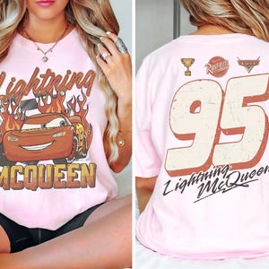 May include: Pink t-shirt featuring Lightning McQueen from the movie Cars. The front displays the character with flames and the text "Lightning McQueen". The back shows the number "95" and "Lightning McQueen".