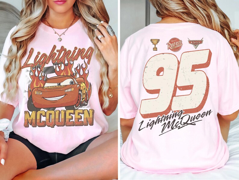 May include: Pink t-shirt featuring Lightning McQueen from the movie Cars. The front displays the character with flames and the text "Lightning McQueen". The back shows the number "95" and "Lightning McQueen".