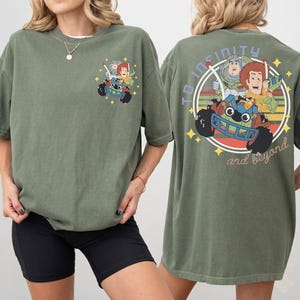 Op de afbeelding: Olijfgroen T-shirt met een Toy Story-afbeelding op de voor- en achterkant. Het ontwerp op de achterkant toont de tekst "To Infinity and Beyond" in een cirkel. Het shirt heeft een relaxte, oversized pasvorm, ideaal voor casual wear.