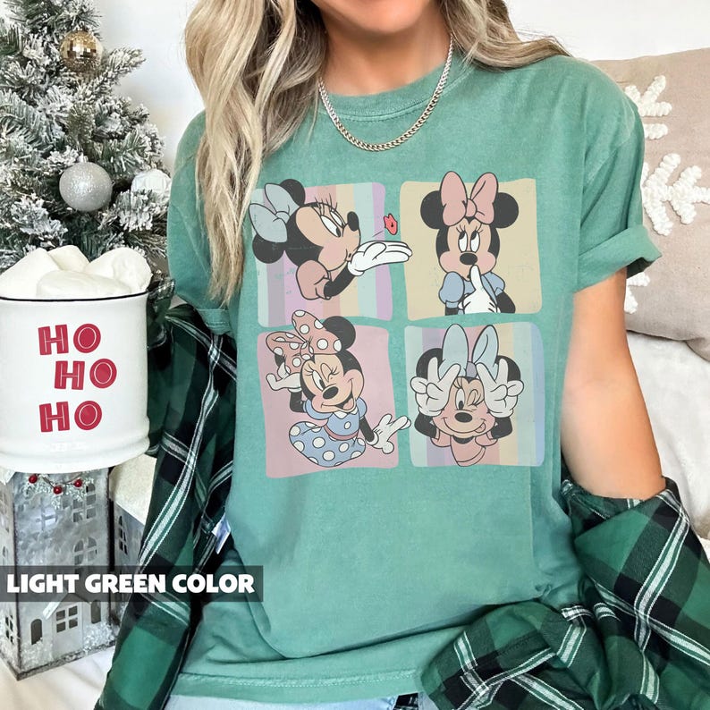 May include: Light green t-shirt featuring a four-panel graphic of Minnie Mouse in various poses. The shirt has rolled-up sleeves and the text "LIGHT GREEN COLOR" at the bottom. The shirt is a comfortable, casual style.