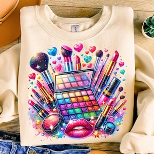 May include: A cream-colored sweatshirt with a colorful graphic design of makeup brushes, lipstick, eyeshadow palettes, and hearts. The design is surrounded by a sparkly, iridescent background.