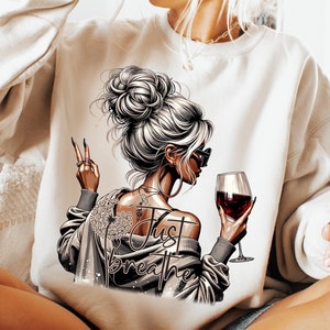 以下が含まれることがあります： 赤いワイングラスを持ったお団子ヘアの女性が描かれた白いスウェットシャツ。スウェットシャツには「Just Breathe」の文字がプリントされています。