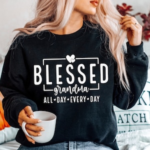 Op de afbeelding: Zwart sweatshirt met witte tekst die "Blessed grandma all day every day" zegt met een hartgrafiek.