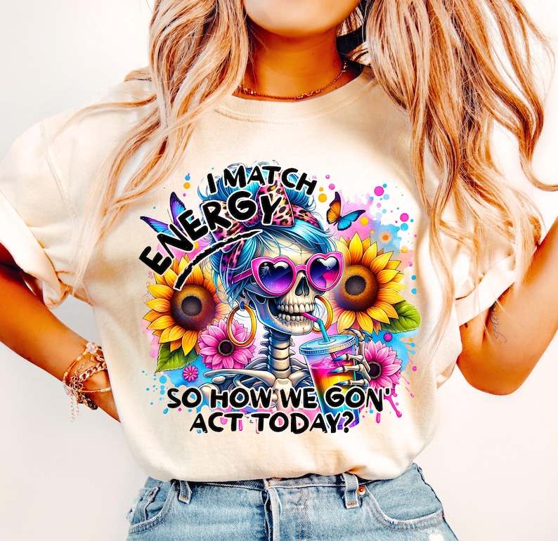 May include: A white t-shirt with a colorful graphic of a skeleton wearing sunglasses and a headband. The graphic includes the text "I Match Energy So How We Gon' Act Today?"