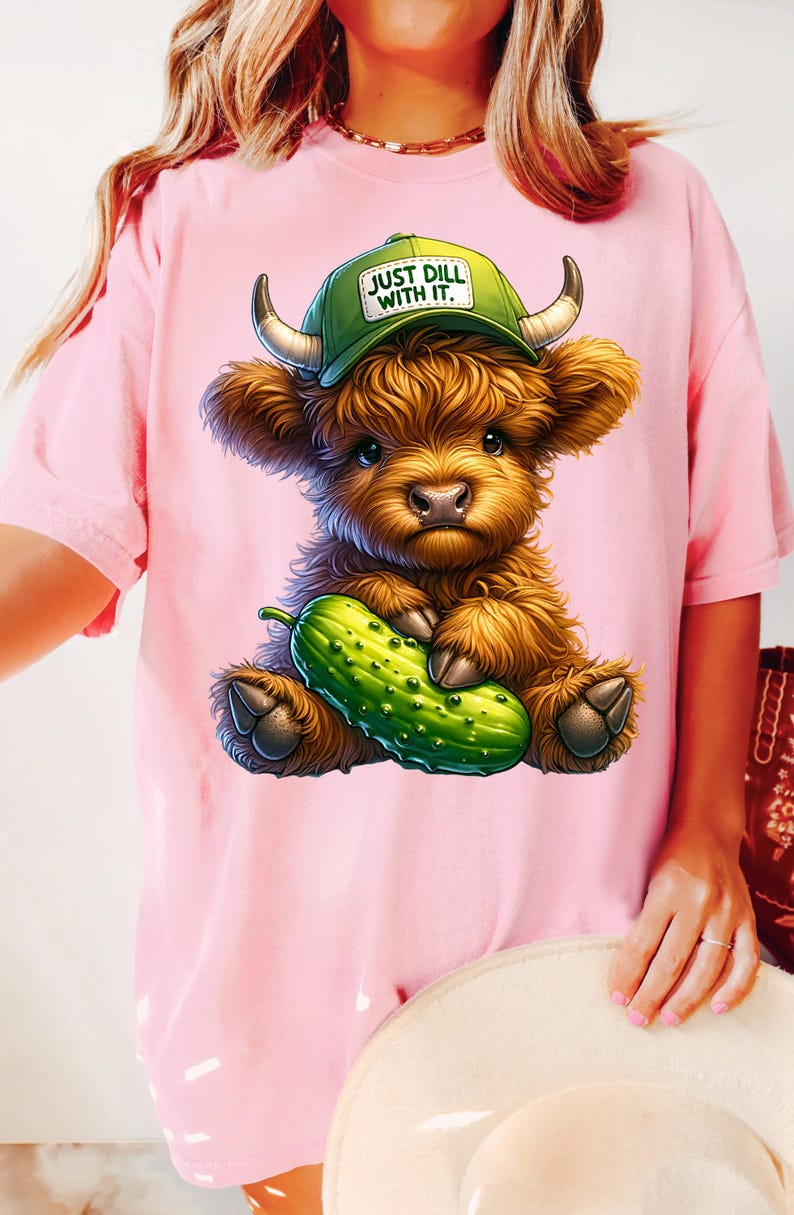 May include: Pink t-shirt with a cartoon Highland cow wearing a green baseball cap that says "Just Dill With It." The cow is holding a green pickle.