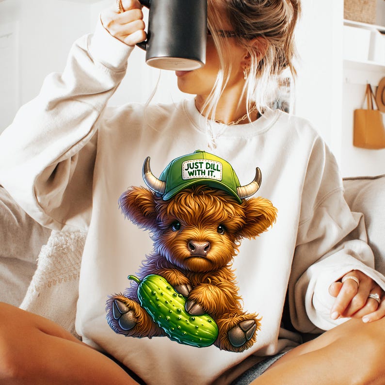 May include: White sweatshirt with a cartoon highland cow wearing a green baseball cap that says "Just Dill With It." The cow is holding a green pickle.