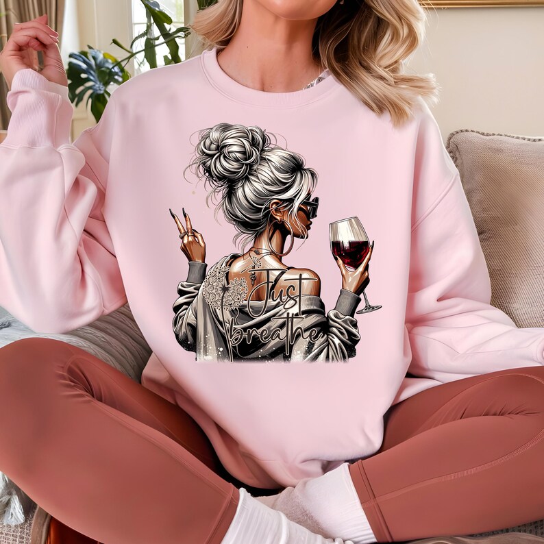 Peut inclure: Sweat-shirt rose avec un motif repr&eacute;sentant une femme avec un verre de vin et le texte "Just Breathe".