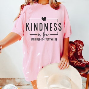 May include: Pink t-shirt with the text "KINDNESS is free SPRINKLE IT EVERYWHERE" in a black box with two small hearts above the text.