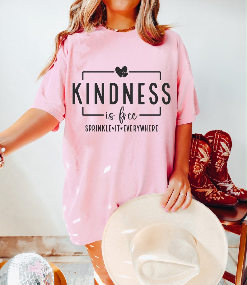May include: Pink t-shirt with the text "KINDNESS is free SPRINKLE IT EVERYWHERE" in a black box with two small hearts above the text.