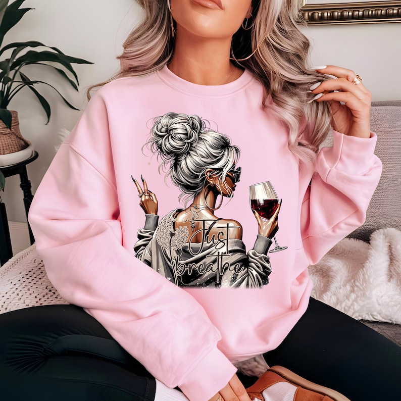 Peut inclure: Sweat-shirt rose avec un motif repr&eacute;sentant une femme avec un verre de vin et le texte "Just Breathe".