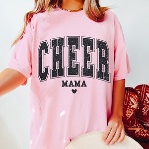 May include: Pink t-shirt with a black distressed graphic that says "CHEER MAMA" with a small heart below the text.