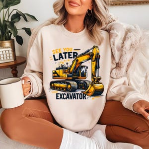 May include: A cream-colored sweatshirt with a yellow excavator graphic and the text "See You Later Excavator".