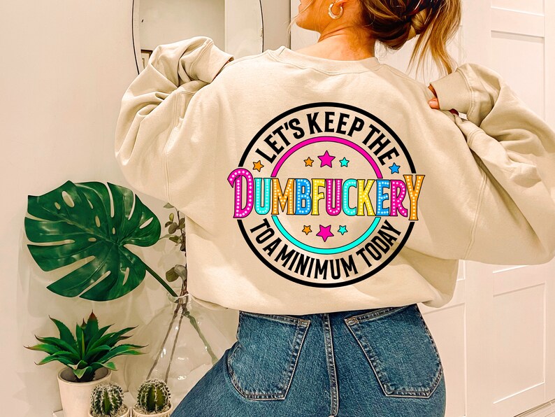 May include: A beige sweatshirt with a colorful graphic print that says "Let's Keep the Dumbfuckery to a Minimum Today".