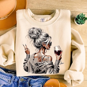 Peut inclure: Un sweat-shirt beige avec un motif repr&eacute;sentant une femme tenant un verre de vin rouge et le texte "Just Breathe".