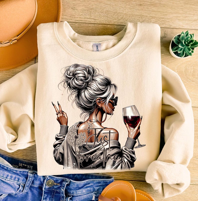 Peut inclure: Un sweat-shirt beige avec un motif repr&eacute;sentant une femme tenant un verre de vin rouge et le texte "Just Breathe".