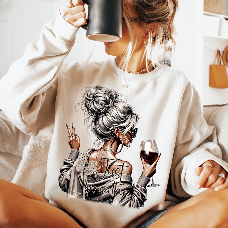 Peut inclure: Sweat-shirt blanc avec un motif repr&eacute;sentant une femme avec un chignon tenant un verre de vin rouge. Le texte "Just Breathe" est imprim&eacute; sur le sweat-shirt.
