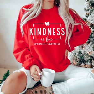 May include: Red sweatshirt with white text that reads "KINDNESS is free SPRINKLE IT EVERYWHERE" with a small heart graphic.