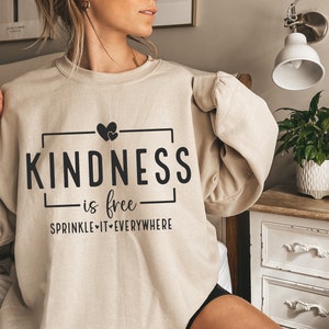 May include: A beige sweatshirt with the text "KINDNESS is free SPRINKLE IT EVERYWHERE" and two small hearts above the word "KINDNESS".