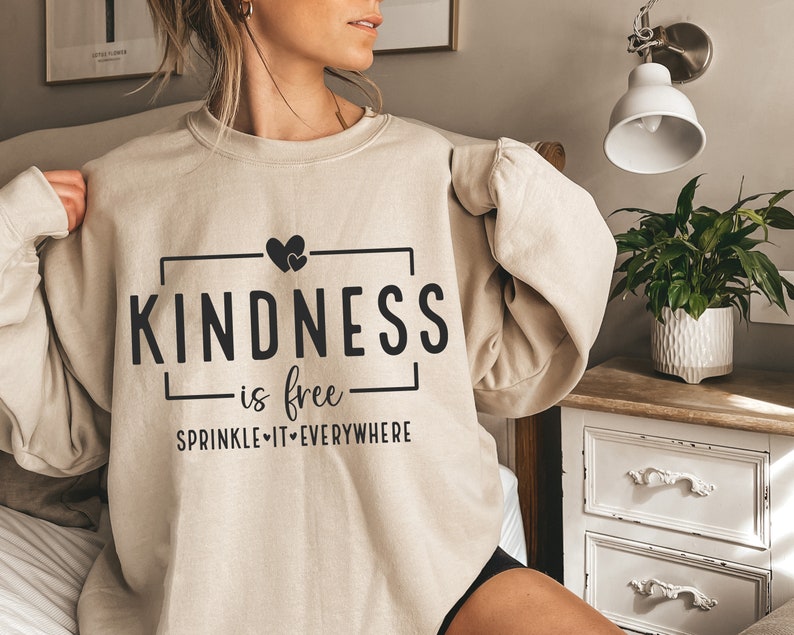 May include: A beige sweatshirt with the text "KINDNESS is free SPRINKLE IT EVERYWHERE" and two small hearts above the word "KINDNESS".