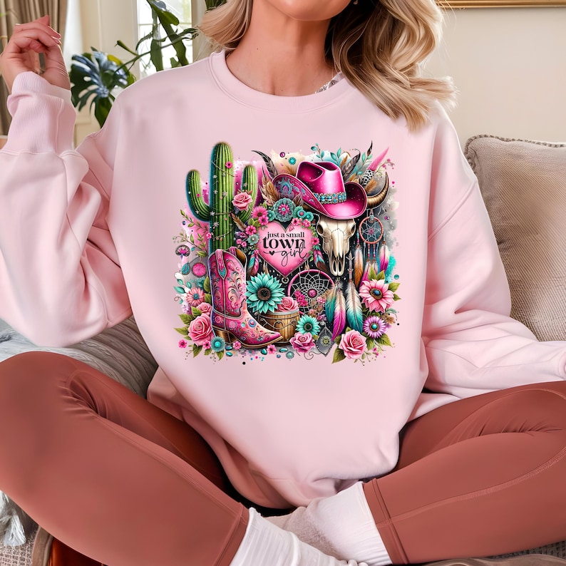 May include: Pink sweatshirt with a graphic design of a cactus, a cowboy hat, a skull, a boot, and flowers. The text "Just a small town girl" is on a pink heart.