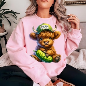 May include: Pink sweatshirt with a cartoon highland cow wearing a green hat that says "Just Dill With It." The cow is holding a green pickle.