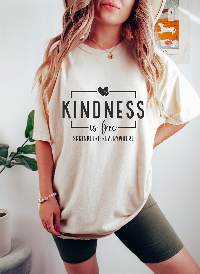 May include: A white t-shirt with a black graphic that says "Kindness is free - Sprinkle it everywhere" with two hearts above the word "Kindness".